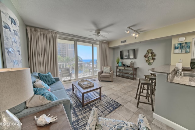 living area with light tile patterned floors, visible vents, baseboards, ceiling fan, and a textured ceiling