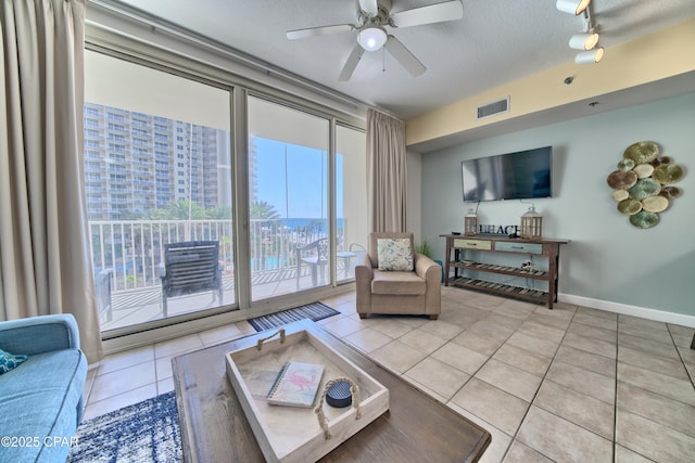 tiled living room featuring a textured ceiling, baseboards, visible vents, ceiling fan, and expansive windows