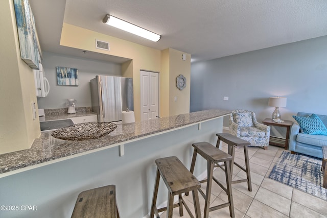 kitchen with dark stone countertops, a breakfast bar area, visible vents, light tile patterned flooring, and freestanding refrigerator