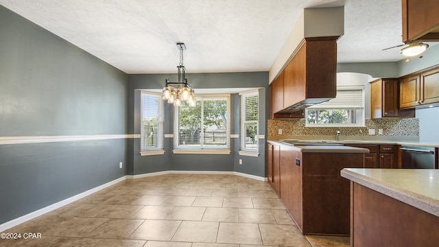 kitchen featuring baseboards, backsplash, hanging light fixtures, stainless steel dishwasher, and a sink