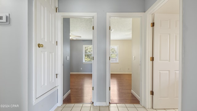 hallway with a textured ceiling, baseboards, and light tile patterned floors