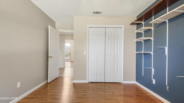 unfurnished bedroom with a closet, wood finished floors, visible vents, and baseboards