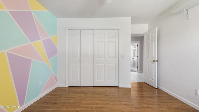 unfurnished bedroom with a closet, wood finished floors, and baseboards