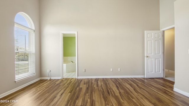 empty room featuring a towering ceiling, baseboards, and wood finished floors