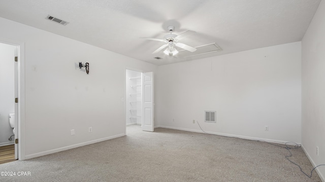 unfurnished room with light carpet, attic access, visible vents, and a ceiling fan