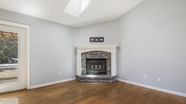 unfurnished living room featuring lofted ceiling with skylight, a tiled fireplace, wood finished floors, and baseboards