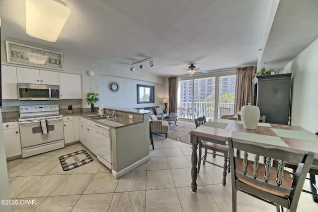 kitchen with a peninsula, white appliances, white cabinetry, a ceiling fan, and a sink