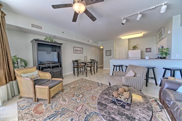 living room featuring visible vents, baseboards, ceiling fan, light tile patterned flooring, and a textured ceiling