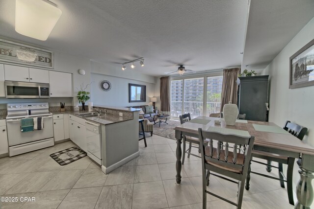 kitchen with a sink, white cabinetry, white appliances, a peninsula, and ceiling fan