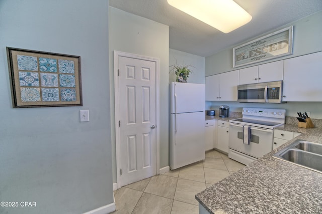 kitchen featuring white appliances, light tile patterned floors, baseboards, a sink, and white cabinets