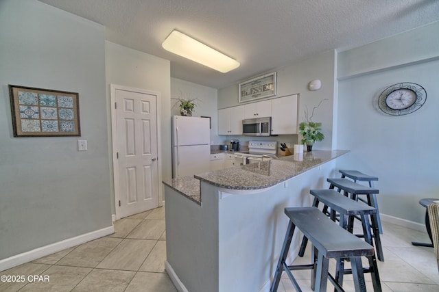 kitchen featuring a breakfast bar, stone counters, a peninsula, white appliances, and white cabinetry