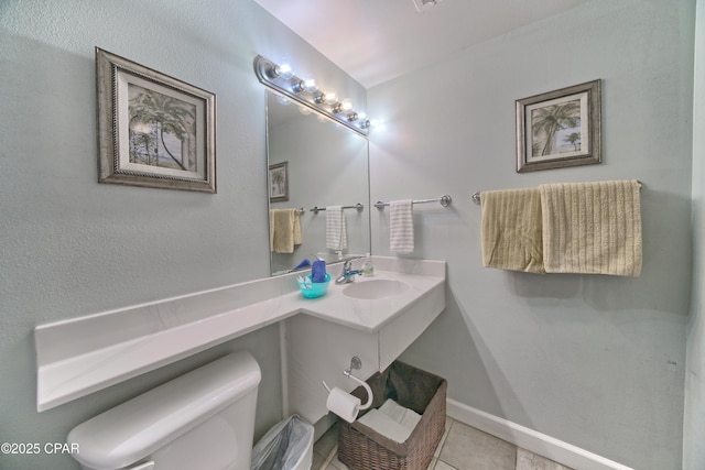 half bath with baseboards, toilet, vanity, and tile patterned flooring