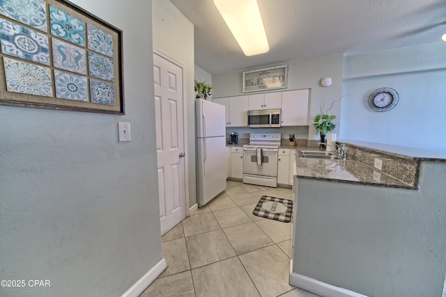 kitchen with a sink, white cabinetry, white appliances, a peninsula, and light tile patterned floors