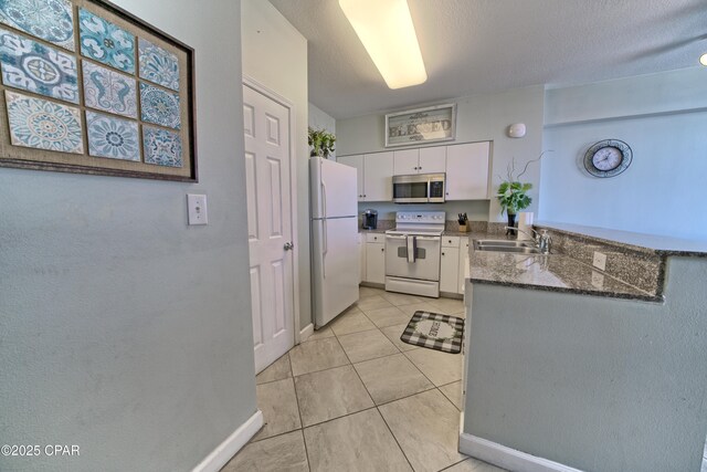 kitchen with light tile patterned floors, a peninsula, white appliances, white cabinetry, and a sink
