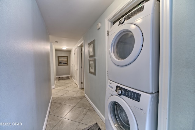 clothes washing area with light tile patterned floors, stacked washer / drying machine, baseboards, and laundry area