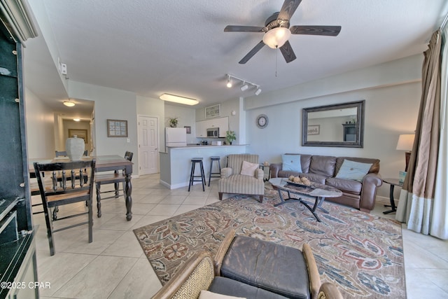 living area with light tile patterned flooring, a ceiling fan, baseboards, and a textured ceiling