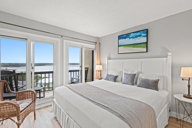 bedroom with light wood-type flooring, access to exterior, a water view, and a textured ceiling