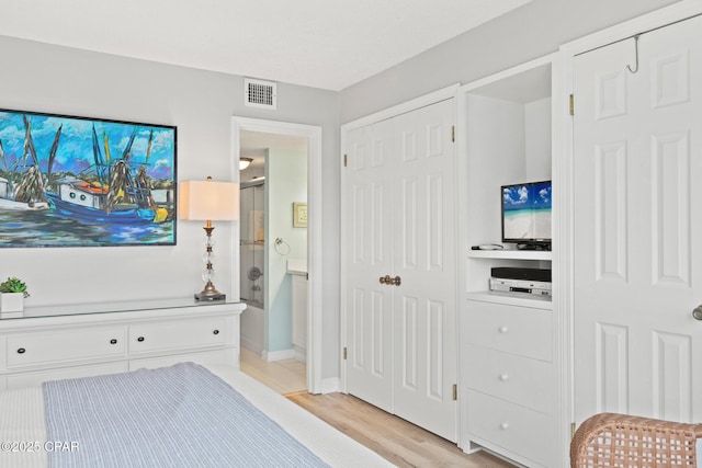 bedroom featuring light wood-style floors, visible vents, and connected bathroom