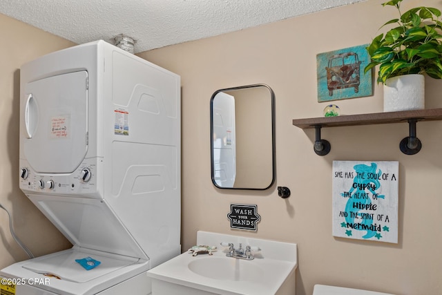 half bathroom with a textured ceiling, stacked washing maching and dryer, a sink, and toilet