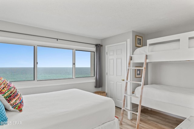 bedroom with a textured ceiling, a water view, and wood finished floors