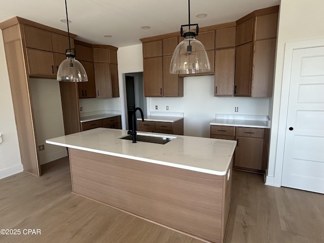 kitchen featuring a sink, light wood-style floors, an island with sink, and hanging light fixtures