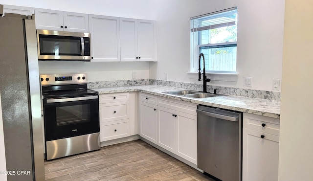 kitchen with wood tiled floor, light stone counters, appliances with stainless steel finishes, white cabinetry, and a sink