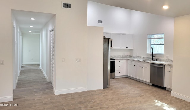 kitchen featuring visible vents, a sink, appliances with stainless steel finishes, white cabinetry, and light wood-type flooring