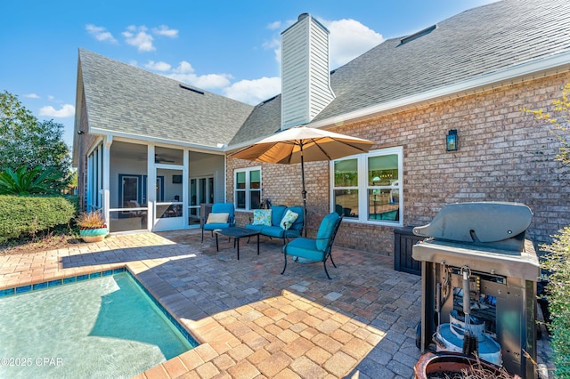 rear view of house with a sunroom, a patio area, brick siding, and roof with shingles
