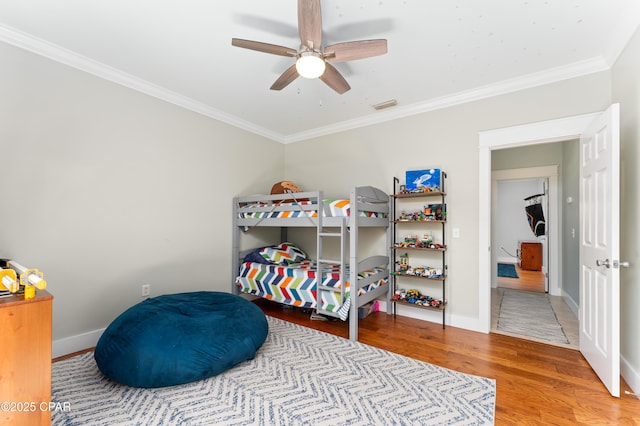 bedroom with ceiling fan, crown molding, visible vents, baseboards, and wood finished floors