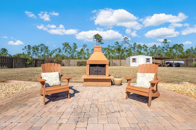 view of patio / terrace featuring an outdoor fireplace, a fenced backyard, a shed, and an outbuilding