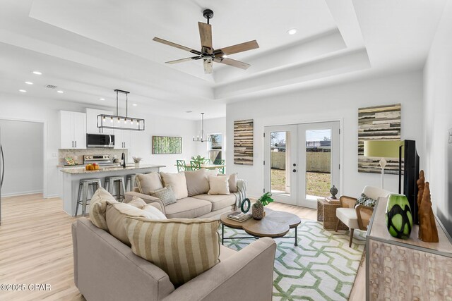 living area with a tray ceiling, french doors, recessed lighting, and light wood-style flooring