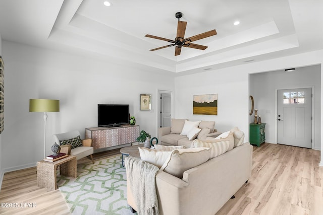 living area with a ceiling fan, recessed lighting, a raised ceiling, light wood finished floors, and baseboards