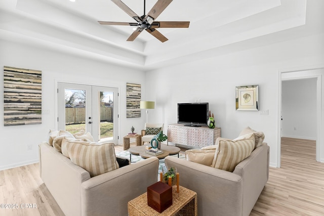 living room featuring baseboards, french doors, a ceiling fan, a tray ceiling, and light wood finished floors