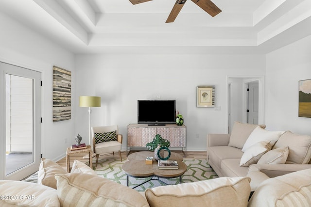 living area with a tray ceiling, baseboards, a ceiling fan, and wood finished floors