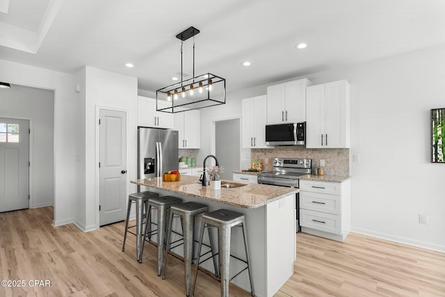 kitchen featuring a kitchen island with sink, light wood-style floors, a kitchen bar, stainless steel appliances, and a sink
