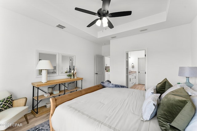 bedroom with a raised ceiling, visible vents, a ceiling fan, and light wood-style flooring