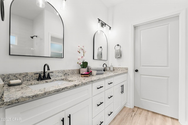 full bathroom featuring wood finished floors, double vanity, a sink, and walk in shower