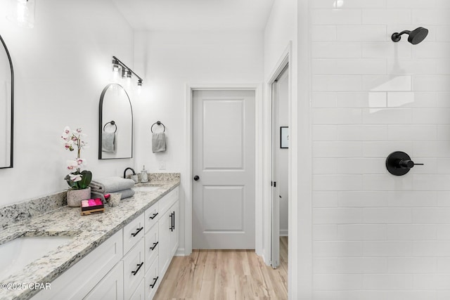 full bath with a sink, double vanity, wood finished floors, and tiled shower
