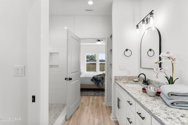 ensuite bathroom with connected bathroom, tiled shower, vanity, a ceiling fan, and wood finished floors