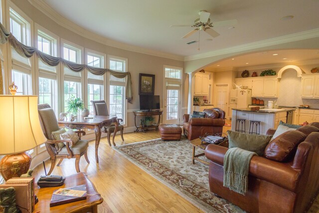 living room featuring visible vents, arched walkways, ceiling fan, crown molding, and light wood-type flooring