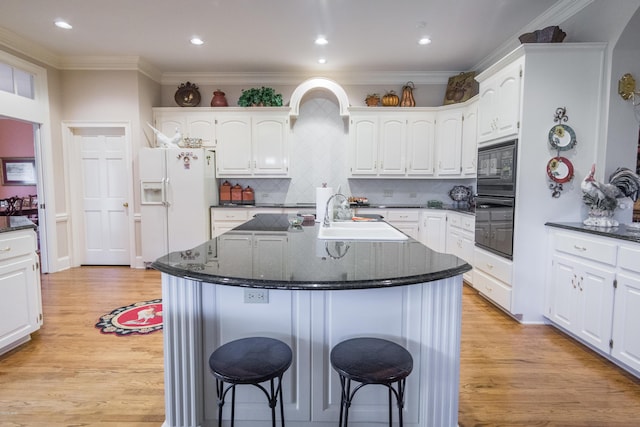 kitchen featuring a kitchen bar, black appliances, white cabinetry, and a sink