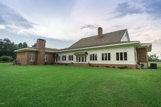 back of house featuring brick siding, a lawn, central AC unit, and a chimney