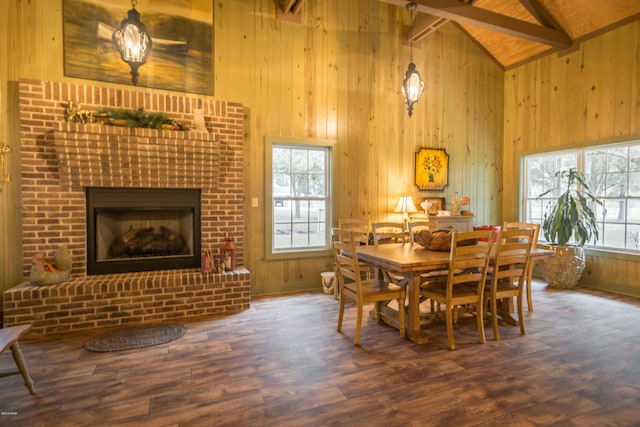 dining space with beamed ceiling, high vaulted ceiling, wood finished floors, wooden walls, and a fireplace