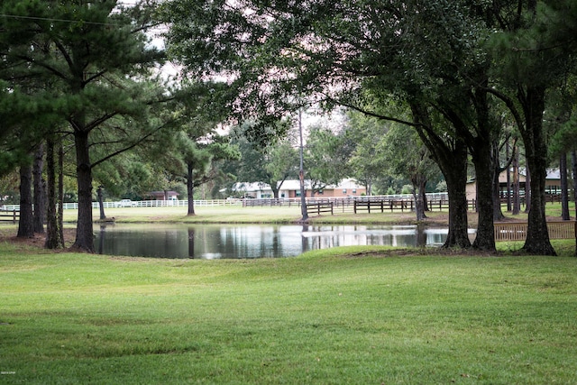 view of home's community with a yard, a water view, and fence