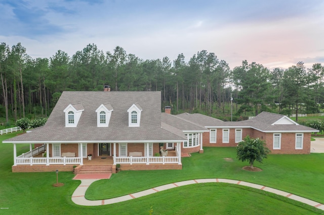 view of front facade featuring brick siding, covered porch, a chimney, and a front lawn