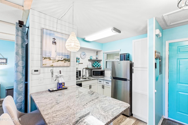 kitchen with light stone countertops, light wood-type flooring, appliances with stainless steel finishes, white cabinetry, and a sink