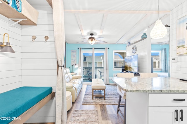 living room featuring a ceiling fan, wooden walls, and wood finished floors