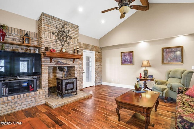 living area featuring a wood stove, ceiling fan, wood finished floors, high vaulted ceiling, and baseboards