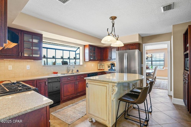 kitchen with a sink, visible vents, backsplash, freestanding refrigerator, and glass insert cabinets