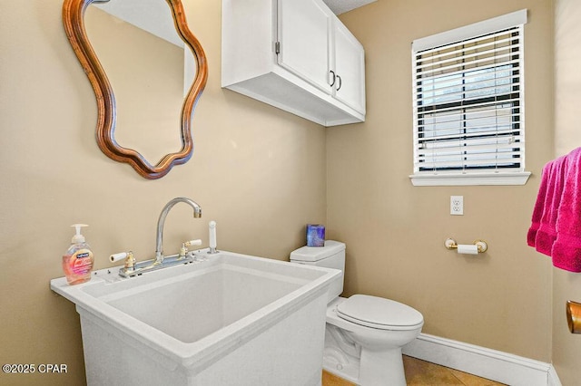 half bathroom with toilet, tile patterned flooring, baseboards, and a sink